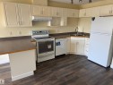 Kitchen with wood-finish flooring, white cabinetry, dark countertops, white appliances, and track lighting - #229 2305 35A Av Nw, Edmonton, AB 