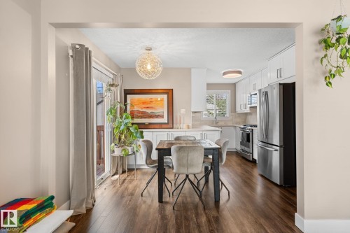 Open concept kitchen and dining area featuring laminate flooring, white cabinetry, stainless steel appliances, and a sliding glass door - 6108 102 Avenue Nw, Edmonton, AB 