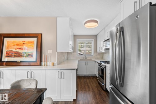 White shaker cabinetry, stainless steel appliances, laminate flooring, white countertops, and a subway tile backsplash - 6108 102 Avenue Nw, Edmonton, AB 