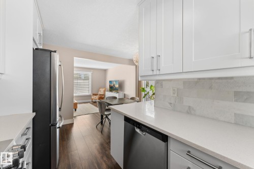 Kitchen featuring white shaker-style cabinetry, stainless steel appliances, light-toned quartz countertops, and a full-height backsplash - 6108 102 Avenue Nw, Edmonton, AB 