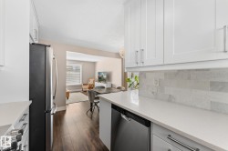 Kitchen featuring white shaker-style cabinetry, stainless steel appliances, light-toned quartz countertops, and a full-height backsplash - 