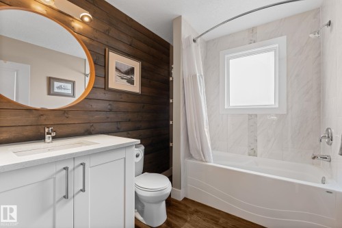 White vanity with integrated sink, laminate flooring, wood plank accent wall, and tiled shower surround with a window - 6108 102 Avenue Nw, Edmonton, AB 
