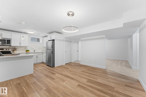 Open-concept dining and kitchen area with vinyl plank flooring, white walls, white cabinetry, stainless steel appliances, and a contemporary ceiling light fixture - 6108 102 Avenue Nw, Edmonton, AB 