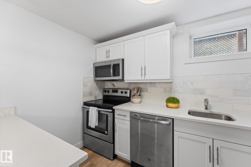 Kitchen featuring vinyl plank flooring, white cabinetry, stainless steel appliances, and a light-toned quartz countertop with a breakfast bar - 6108 102 Avenue Nw, Edmonton, AB 
