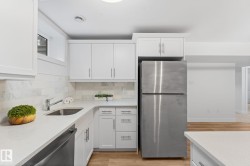Kitchen featuring vinyl plank flooring, white cabinetry, stainless steel appliances, and a light-toned quartz countertop with a breakfast bar - 