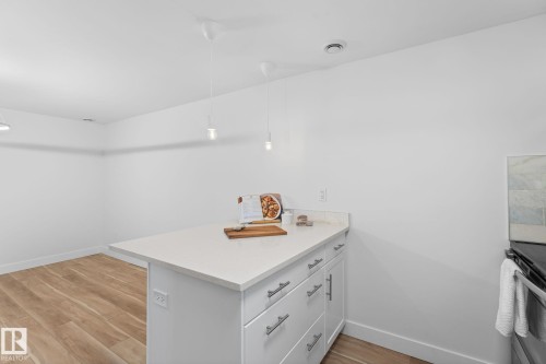 Kitchen featuring vinyl plank flooring, white cabinetry, stainless steel appliances, and a light-toned quartz countertop with a breakfast bar - 6108 102 Avenue Nw, Edmonton, AB 