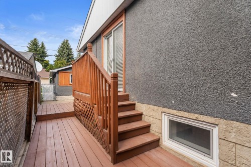 Wood-finish deck with stairs and lattice railing, sliding glass door, textured stucco exterior, and basement window with stone surround - 6108 102 Avenue Nw, Edmonton, AB 
