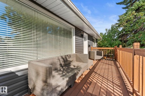 Expansive wooden deck with wood railings, featuring horizontal siding, a large window with blinds, and mature trees in the background - 6108 102 Avenue Nw, Edmonton, AB 