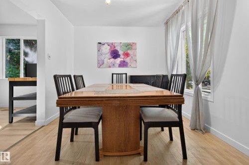 Hardwood-style flooring with white baseboards, bright white walls, and a large window with sheer drapes - 6807 112A Street Nw, Edmonton, AB 
