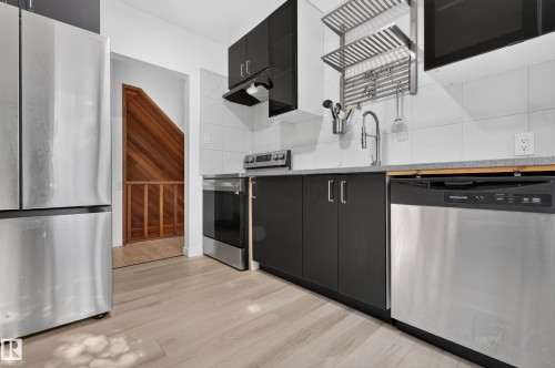 Stainless steel appliances, black flat-panel cabinetry, light wood-finish flooring, white tile backsplash, and a contemporary stainless steel faucet - 6807 112A Street Nw, Edmonton, AB 