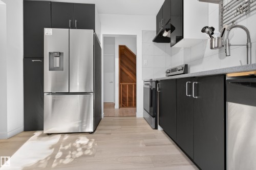 Kitchen featuring stainless steel appliances, dark cabinetry, light wood-finish flooring, and a white tiled backsplash - 6807 112A Street Nw, Edmonton, AB 