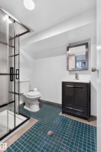 Walk-in shower with a glass enclosure, teal tile flooring, a dark wood-finish vanity, and a wall-mounted mirror - 6807 112A Street Nw, Edmonton, AB 