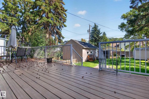 Expansive wood-finish deck with metal railings, overlooking a grassy yard with mature trees and a detached shed - 6807 112A Street Nw, Edmonton, AB 