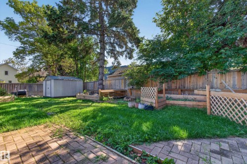 Expansive backyard featuring a brick paver patio, a manicured lawn, a storage shed, and raised garden beds - 6807 112A Street Nw, Edmonton, AB 