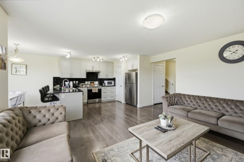 Open-concept living area with wood-finish flooring, white cabinetry, a black subway tile backsplash, and stainless steel appliances - 941 Ebbers Crescent Nw, Edmonton, AB 