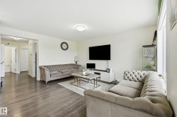 Spacious living area featuring wood-finish flooring, light-colored walls, and a ceiling-mounted light fixture - 