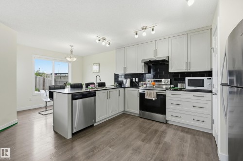 Modern kitchen featuring light gray cabinetry, black subway tile backsplash, stainless steel appliances, and wood-finish flooring - 941 Ebbers Crescent Nw, Edmonton, AB 