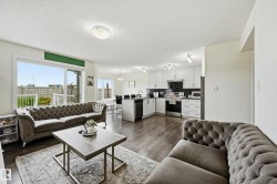 Open-concept living area with dark wood-finish flooring, a contemporary kitchen featuring white cabinetry, dark backsplash, and stainless steel appliances, and a dining area with a modern chandelier - 