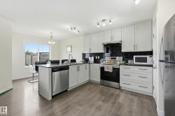 Modern kitchen featuring light gray cabinetry, black subway tile backsplash, stainless steel appliances, and wood-finish flooring - 
