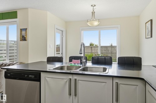 Central island with an undermount double basin sink, stainless steel dishwasher, and dark countertop - 941 Ebbers Crescent Nw, Edmonton, AB 