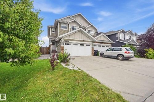 Two-story residence featuring a multi-gable roofline, neutral siding, stone accents, and a dual-bay garage with white doors - 941 Ebbers Crescent Nw, Edmonton, AB 