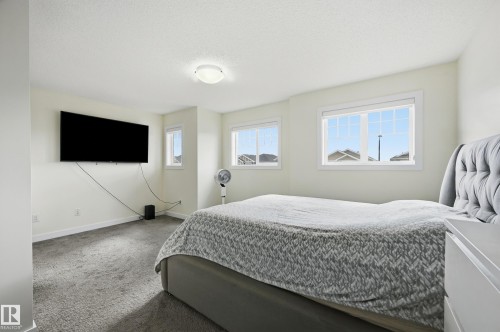Carpeted room featuring multiple windows, a ceiling-mounted light fixture, and a wall-mounted television - 941 Ebbers Crescent Nw, Edmonton, AB 