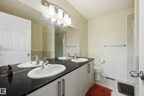 Dual basin vanity with a dark countertop and integrated sinks, illuminated by a contemporary light fixture - 941 Ebbers Crescent Nw, Edmonton, AB 