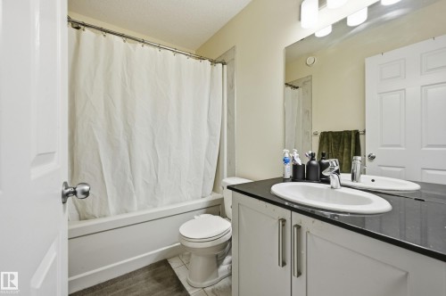 Bathroom featuring a built-in tub with shower, single vanity with dark countertop, and integrated mirror with overhead lighting - 941 Ebbers Crescent Nw, Edmonton, AB 