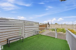 Outdoor patio featuring artificial turf, white horizontal slat fencing, white metal railing, and a sloped garden area - 