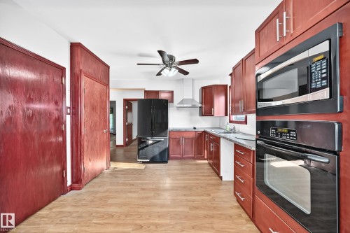 Kitchen featuring wood-finish flooring, cherry-toned cabinetry, stainless steel appliances, and a ceiling fan - 9719 71 Avenue Nw, Edmonton, AB - Indoor Photo Showing Kitchen