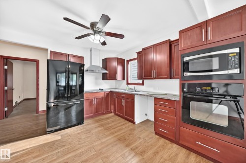 Kitchen featuring wood-finish flooring, cherry-toned cabinetry, stainless steel range hood, built-in microwave, and built-in oven - 9719 71 Avenue Nw, Edmonton, AB - Indoor Photo Showing Kitchen With Double Sink