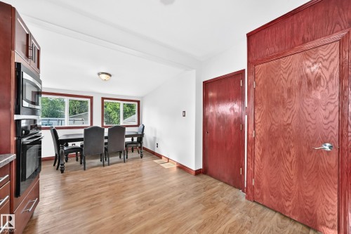 Open-concept dining area featuring wood-finish flooring and multiple windows, complemented by built-in kitchen cabinetry with a wall oven and microwave - 9719 71 Avenue Nw, Edmonton, AB - Indoor