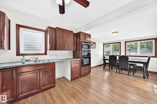 Open-concept kitchen and dining area featuring rich wood cabinetry, integrated wall oven and microwave, dual-basin stainless steel sink, and wood-finish flooring - 9719 71 Avenue Nw, Edmonton, AB - Indoor Photo Showing Kitchen With Double Sink