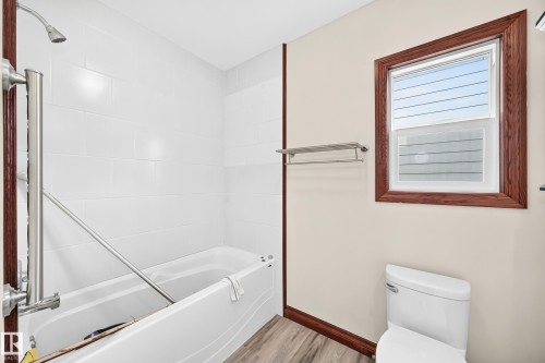 Bathroom featuring a white tiled shower and tub combination, wood-finish flooring, a toilet, and a window with wood trim - 9719 71 Avenue Nw, Edmonton, AB - Indoor Photo Showing Bathroom