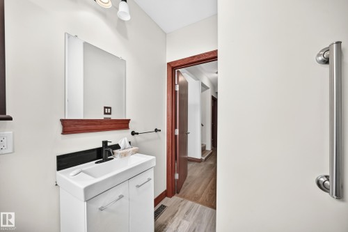 Vanity area featuring a modern white cabinet with integrated sink, matte black faucet, and a wall-mounted mirror with a decorative wood shelf - 9719 71 Avenue Nw, Edmonton, AB - Indoor Photo Showing Bathroom
