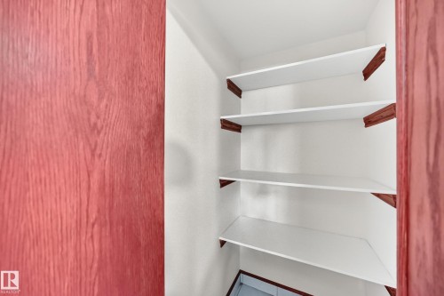 Built-in shelving unit featuring five white shelves with wood-finish supports, framed by a red wood-grain door - 9719 71 Avenue Nw, Edmonton, AB - Indoor With Storage