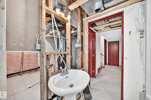 Pedestal sink with chrome faucet, exposed framing, and red-stained interior doorways - 9719 71 Avenue Nw, Edmonton, AB - Indoor Photo Showing Bathroom