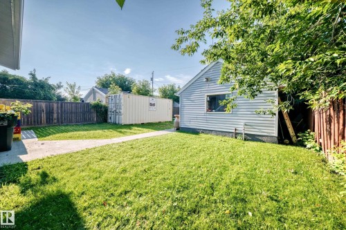 Spacious backyard featuring a manicured lawn, concrete patio, and a detached vinyl-sided structure - 9719 71 Avenue Nw, Edmonton, AB - Outdoor