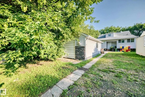 Rear exterior featuring a detached structure with siding and stone veneer, a concrete walkway, and a spacious grassy area leading to the main residence - 9719 71 Avenue Nw, Edmonton, AB - Outdoor