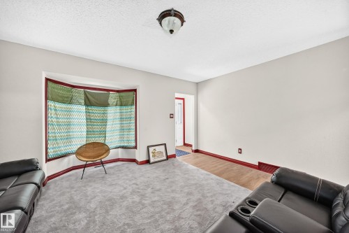 Living space featuring a prominent bay window with deep red trim, light-toned walls, and a textured ceiling - 9719 71 Avenue Nw, Edmonton, AB - Indoor