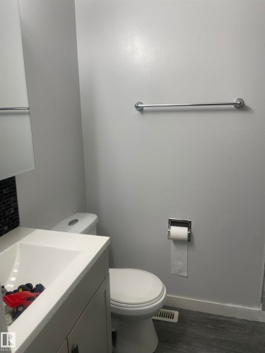 White vanity with integrated sink, chrome hardware, toilet, and wood-finish flooring - 3221 132A Avenue Nw, Edmonton, AB 