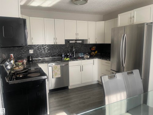 White cabinetry, black mosaic tile backsplash, dark countertops, stainless steel appliances, and wood-finish flooring - 3221 132A Avenue Nw, Edmonton, AB 