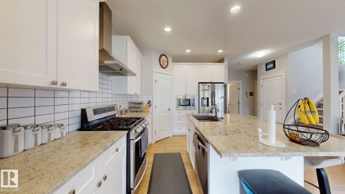 Kitchen featuring white upper and lower cabinetry, light-toned granite countertops, stainless steel appliances, and a white subway tile backsplash - 22407 99 Avenue Nw, Edmonton, AB 