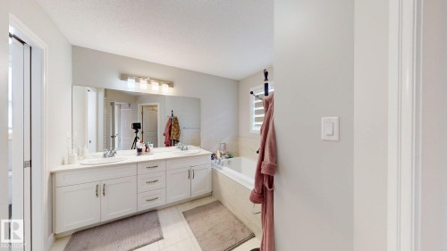 Dual vanity with white cabinetry, built-in bathtub, large wall-mounted mirror, and tile flooring - 22407 99 Avenue Nw, Edmonton, AB 