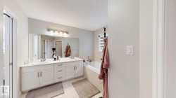 Dual vanity with white cabinetry, built-in bathtub, large wall-mounted mirror, and tile flooring - 