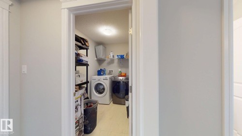 Laundry area with front-loading washer and dryer, wall-mounted shelving, and overhead lighting - 22407 99 Avenue Nw, Edmonton, AB 