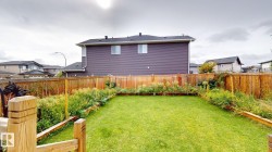 Expansive backyard featuring a manicured lawn, established garden beds, and a wood privacy fence - 