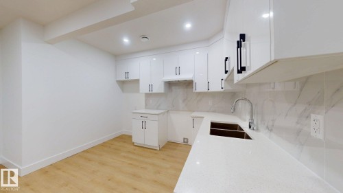 White cabinetry with black hardware, stone countertops, integrated sink with gooseneck faucet, light wood-finish flooring, and recessed ceiling lighting - 22407 99 Avenue Nw, Edmonton, AB 