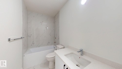 White bathtub with tiled surround, white toilet, vanity with integrated sink, and chrome faucet - 22407 99 Avenue Nw, Edmonton, AB 