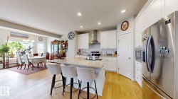 Kitchen island with light-toned countertop, stainless steel appliances, white cabinetry, and wood-finish flooring - 